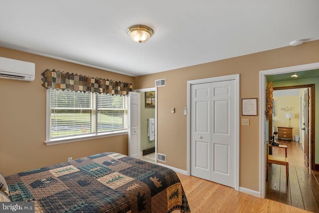 bedroom featuring light wood finished floors, a closet, visible vents, a wall mounted air conditioner, and baseboards