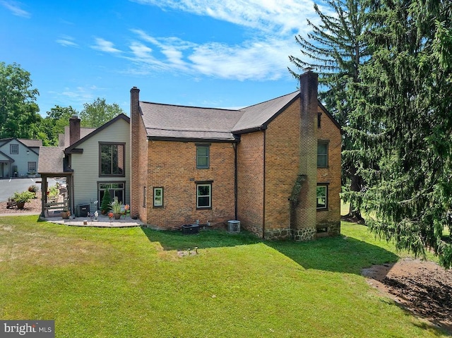 back of property featuring a lawn, a chimney, cooling unit, a patio area, and brick siding