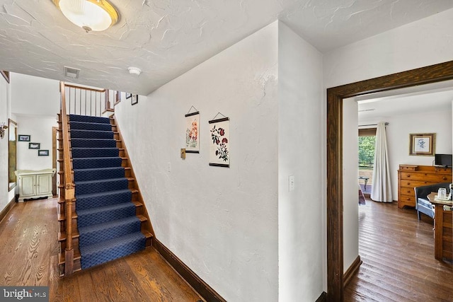 staircase featuring a textured wall, hardwood / wood-style floors, and baseboards