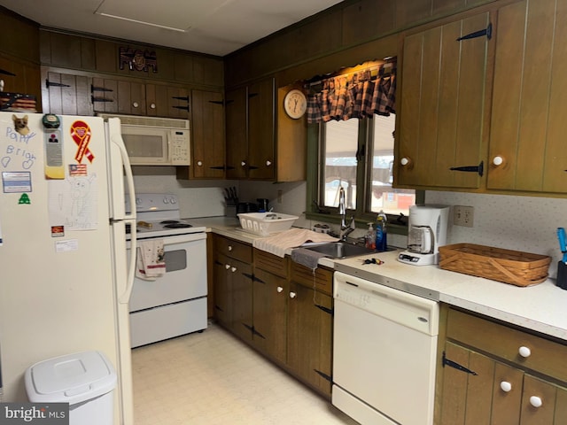 kitchen with dark brown cabinetry, white appliances, a sink, light countertops, and light floors