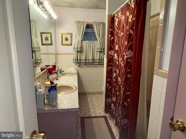 full bath with tile walls, double vanity, curtained shower, wainscoting, and a sink