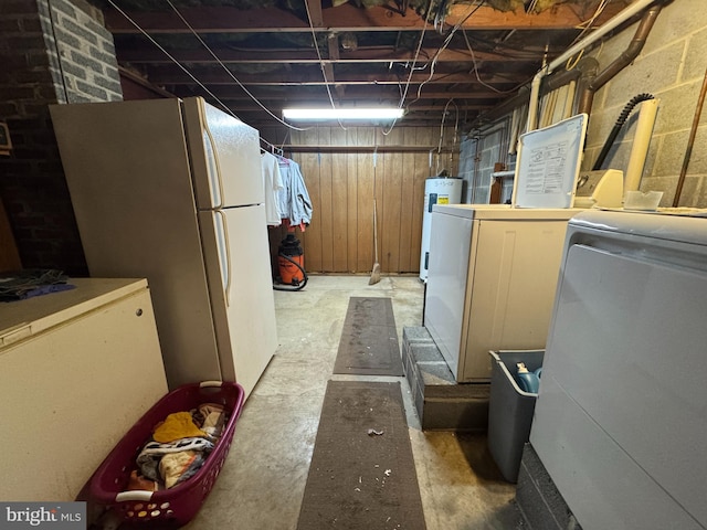 unfinished below grade area featuring electric water heater, washing machine and clothes dryer, and freestanding refrigerator