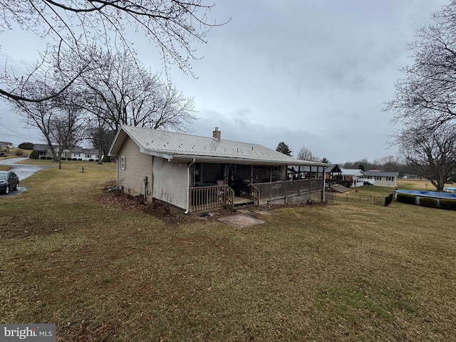 back of house with metal roof, a chimney, and a lawn