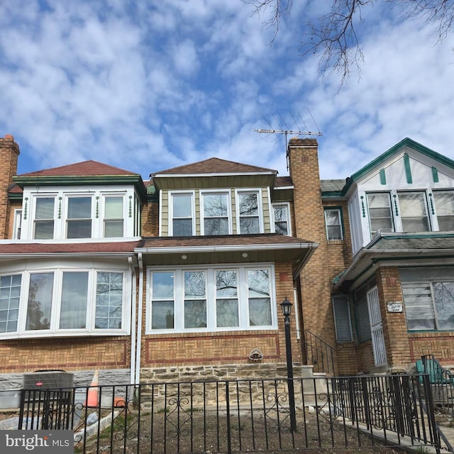 townhome / multi-family property with a fenced front yard, a chimney, and brick siding