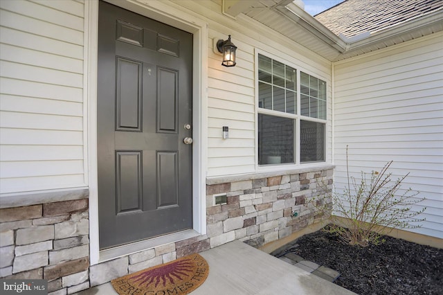 doorway to property featuring a shingled roof and stone siding