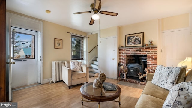 living room with ceiling fan, light wood-style floors, stairs, radiator heating unit, and a wood stove