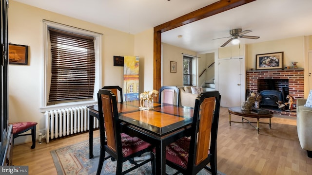 dining room with a ceiling fan, beam ceiling, radiator, light wood finished floors, and a wood stove