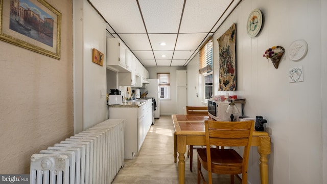 kitchen with light countertops, radiator heating unit, light wood-style floors, white cabinets, and a drop ceiling