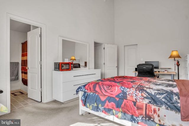 bedroom featuring light carpet, connected bathroom, and a towering ceiling