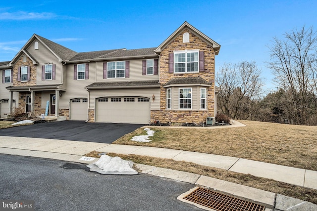 multi unit property with a garage, stone siding, driveway, and a front lawn