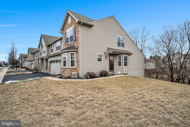 view of side of property with aphalt driveway, a garage, stone siding, a lawn, and a residential view