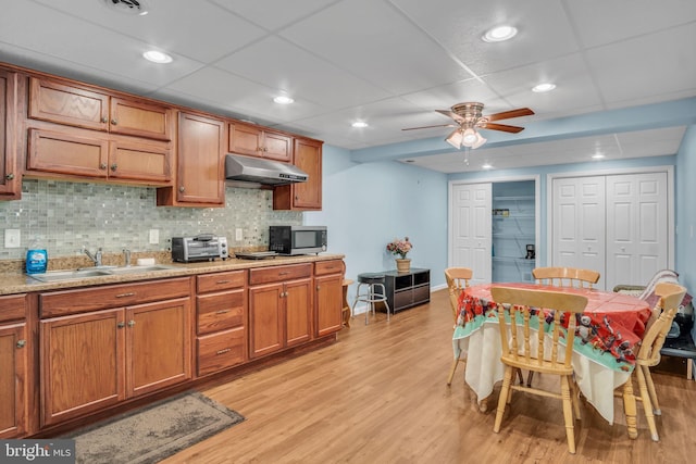 kitchen featuring light wood finished floors, stainless steel microwave, brown cabinetry, a sink, and under cabinet range hood