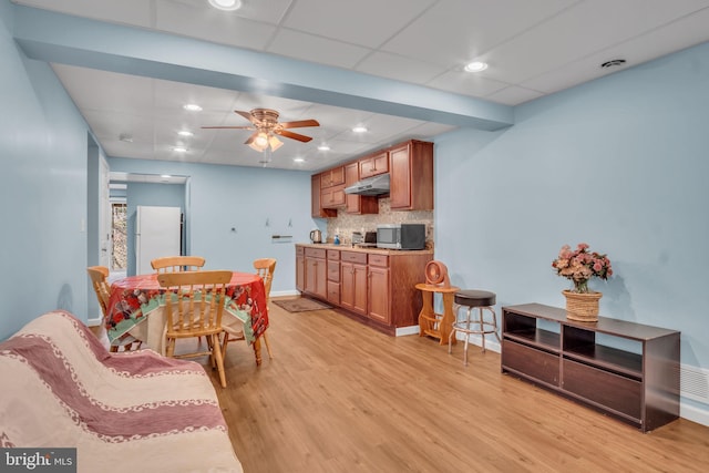 kitchen with under cabinet range hood, light wood-style floors, freestanding refrigerator, decorative backsplash, and stainless steel microwave