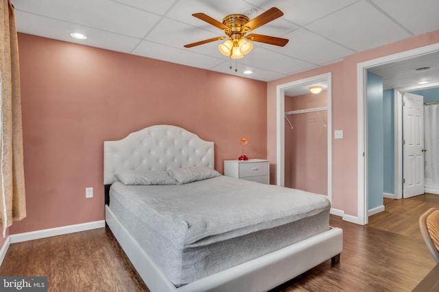 bedroom featuring dark wood-type flooring, a closet, a drop ceiling, and baseboards