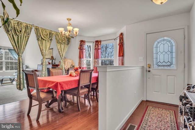 dining space featuring baseboards, wood finished floors, visible vents, and an inviting chandelier