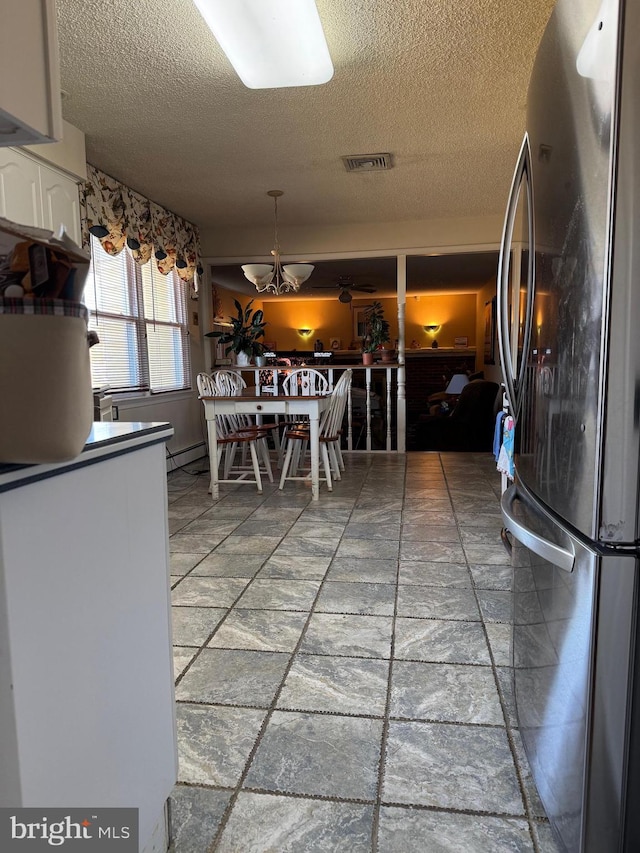 kitchen with a textured ceiling, stone tile floors, visible vents, white cabinetry, and freestanding refrigerator