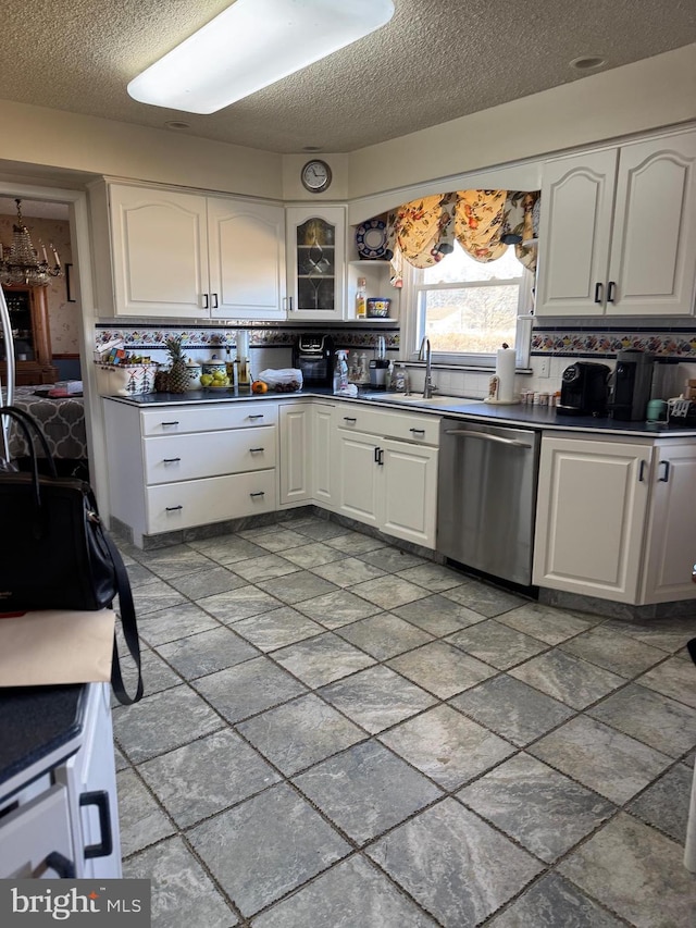 kitchen featuring dark countertops, backsplash, stainless steel dishwasher, white cabinetry, and a sink