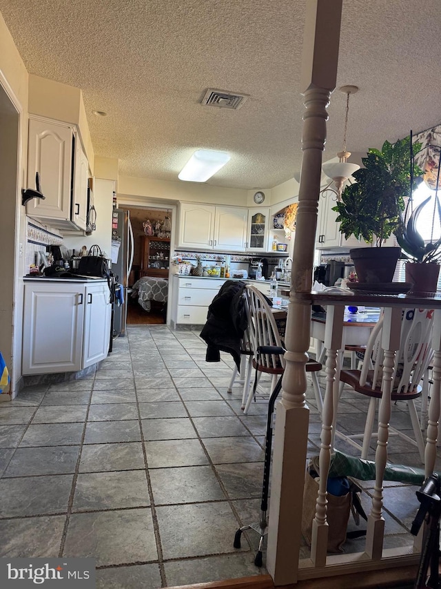 kitchen featuring visible vents, dark countertops, glass insert cabinets, freestanding refrigerator, and white cabinetry