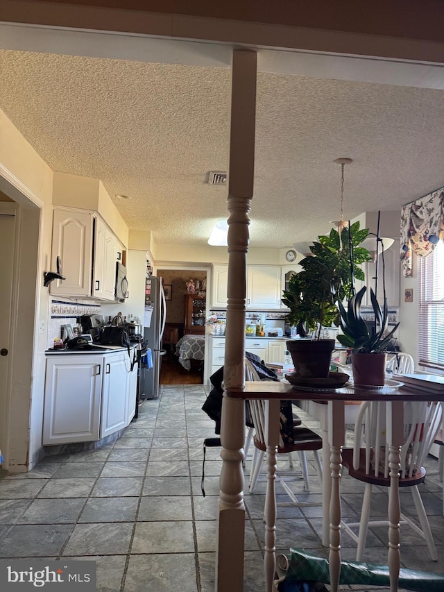 kitchen featuring visible vents, white cabinets, dark countertops, freestanding refrigerator, and a textured ceiling