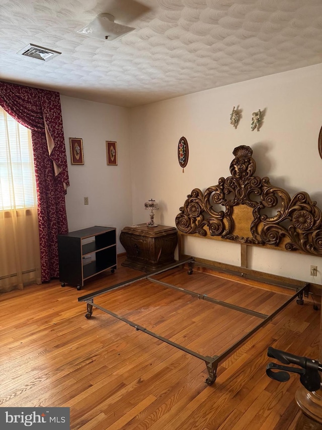 interior space with a textured ceiling, a baseboard heating unit, light wood finished floors, and visible vents