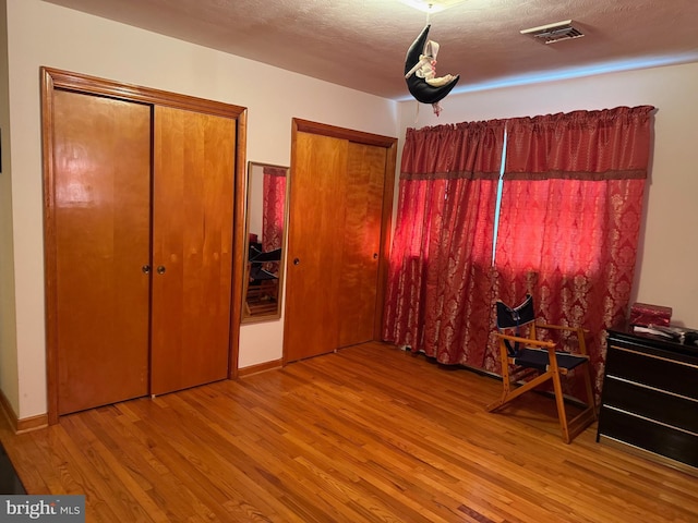 bedroom featuring a textured ceiling, visible vents, two closets, and wood finished floors