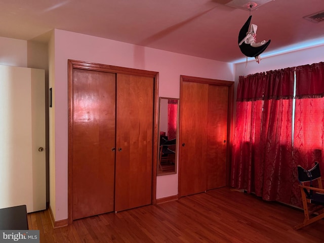 unfurnished bedroom with multiple closets, visible vents, and wood finished floors