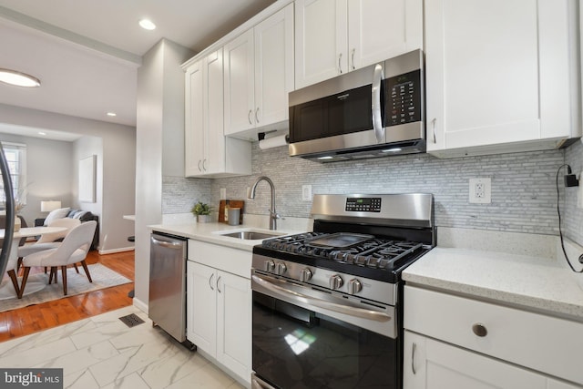 kitchen featuring stainless steel appliances, marble finish floor, white cabinetry, and a sink