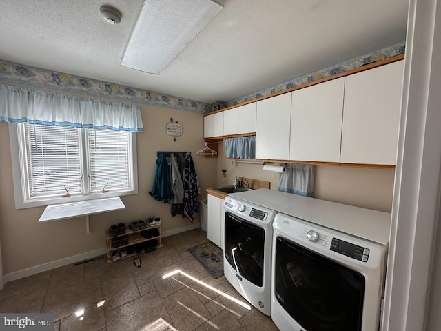 clothes washing area featuring cabinet space, baseboards, a textured ceiling, washing machine and dryer, and a sink