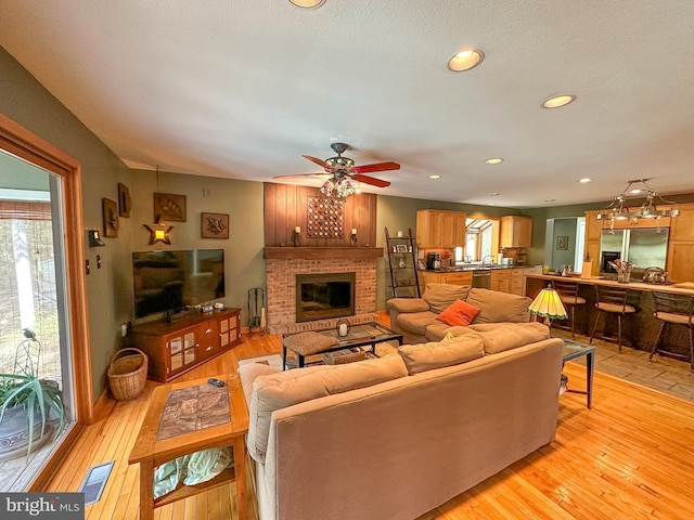 living room featuring light wood-type flooring, a fireplace, visible vents, and recessed lighting