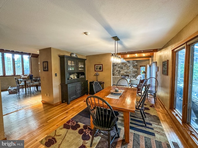 dining room featuring light wood-style floors, visible vents, a textured ceiling, and a stone fireplace