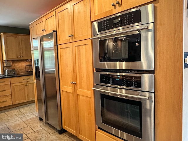 kitchen with appliances with stainless steel finishes, dark countertops, stone finish floor, and backsplash