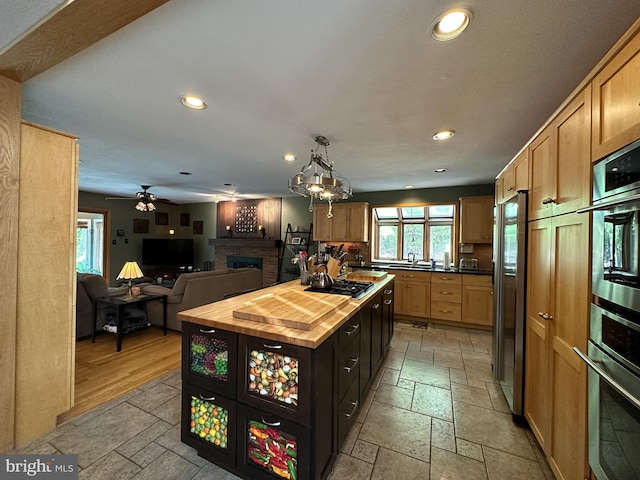 kitchen with recessed lighting, stainless steel appliances, a fireplace, wooden counters, and stone tile flooring