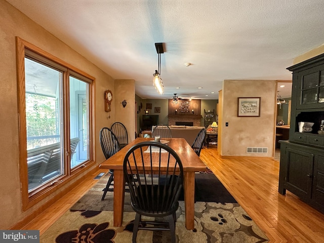 dining area featuring a brick fireplace, visible vents, light wood-style flooring, and a textured ceiling