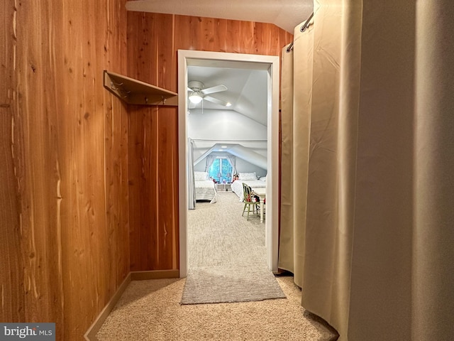 hall featuring wood walls, vaulted ceiling, and carpet flooring