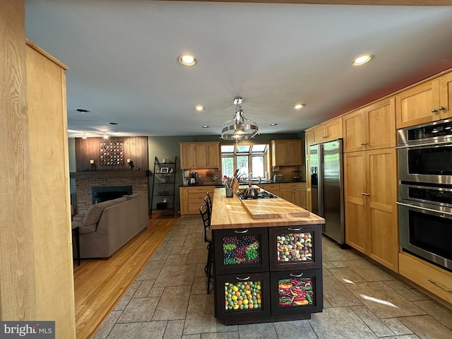 kitchen with stone tile floors, wood counters, appliances with stainless steel finishes, open floor plan, and a fireplace