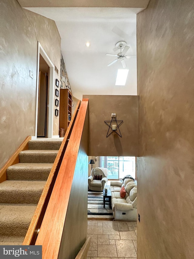 stairway with a towering ceiling, a ceiling fan, and stone tile flooring