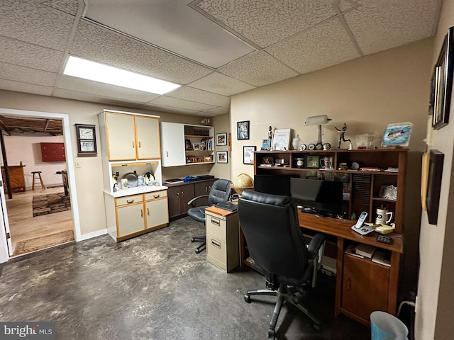 office area featuring concrete flooring, a drop ceiling, and baseboards