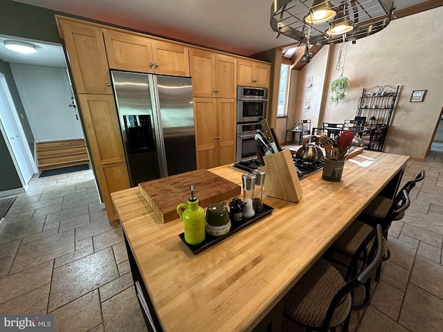 kitchen featuring butcher block countertops, appliances with stainless steel finishes, stone tile flooring, and a breakfast bar area