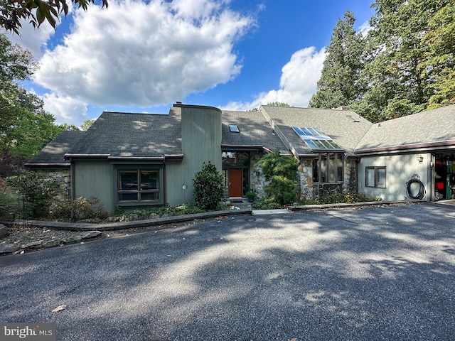 view of front of home featuring uncovered parking, stone siding, and roof with shingles