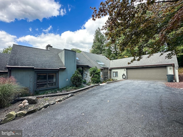 mid-century modern home with a garage, a chimney, aphalt driveway, and roof with shingles