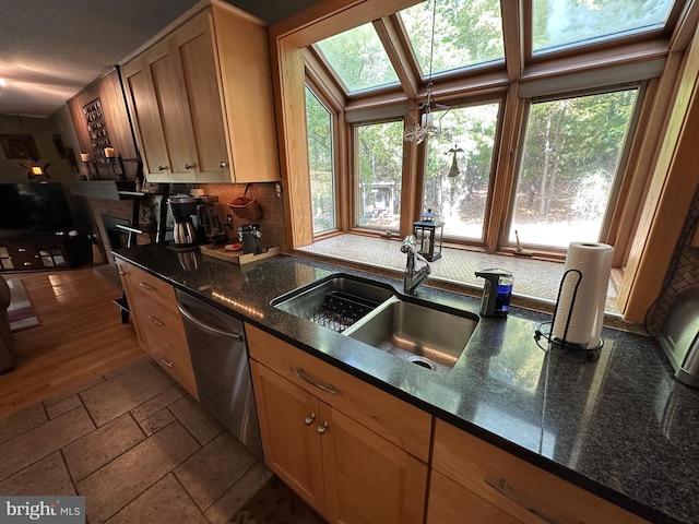 kitchen with stone tile floors, decorative backsplash, dishwasher, dark stone countertops, and a sink