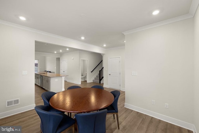 dining room featuring light wood finished floors, baseboards, stairway, and visible vents