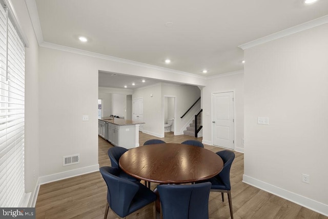 dining room featuring light wood-type flooring, stairway, visible vents, and crown molding