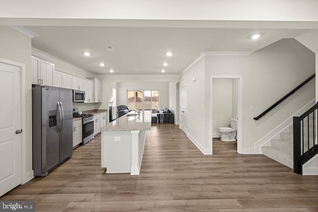 kitchen with light wood finished floors, stainless steel appliances, ornamental molding, white cabinets, and a sink