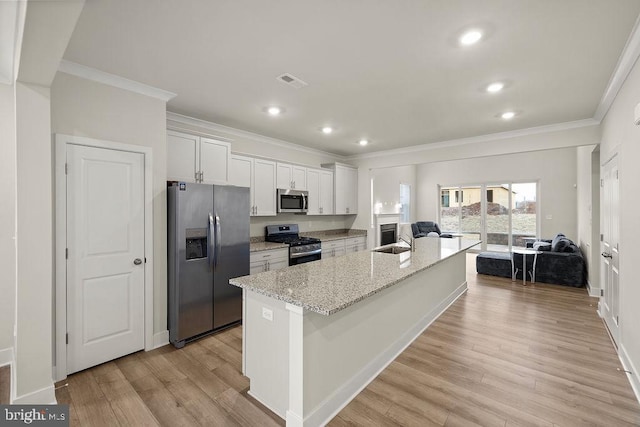 kitchen featuring visible vents, appliances with stainless steel finishes, ornamental molding, a kitchen island with sink, and light wood-style floors