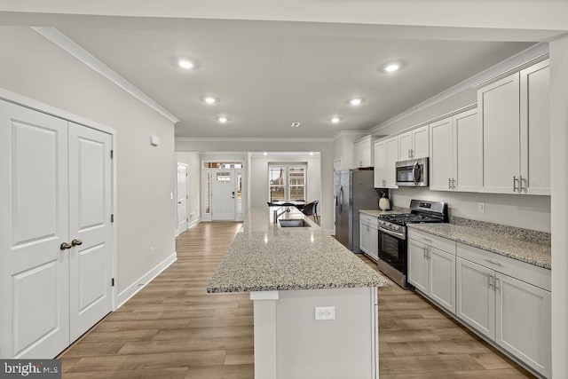 kitchen with light wood finished floors, appliances with stainless steel finishes, ornamental molding, a sink, and an island with sink