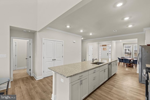 kitchen with light wood finished floors, appliances with stainless steel finishes, an island with sink, and a sink