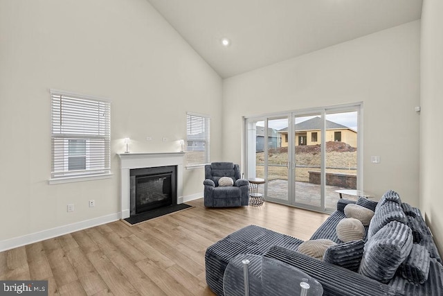 living room with high vaulted ceiling, recessed lighting, a fireplace with flush hearth, baseboards, and light wood finished floors