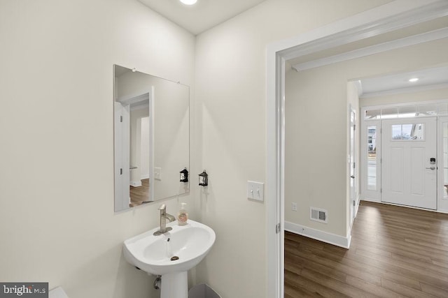 bathroom with baseboards, visible vents, ornamental molding, wood finished floors, and a sink