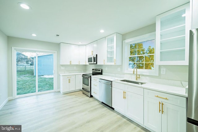 kitchen featuring light wood-type flooring, appliances with stainless steel finishes, white cabinets, and a sink